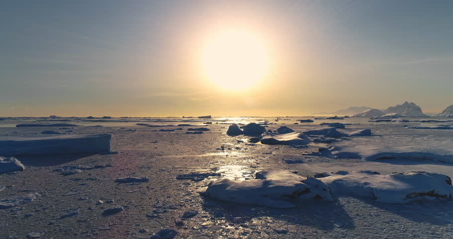 Fly over polar frozen ocean landscape in sunset. Serene beauty of glaciers surrounded by pristine icy snow land. Untouched wilderness of Antarctica. South Pole travel background. Low angle drone shot