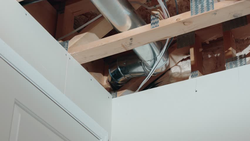 A Long 4K Zoom Shot of the Corner in an Unfinished Basement In a Newly Constructed Built Home Showing Metal HVAC Tubes Two by Four Lumber Drywall Wires Pipes and Insulation Above a White Door.