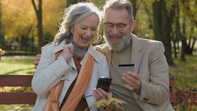 Caucasian couple happy 60s old mature woman man hold credit card mobile phone bank app two grandparents in city park shopping online purchase pay money with smartphone celebrate successful transaction - Powered by Shutterstock - Get 15% off with code: PIKWIZARD15
