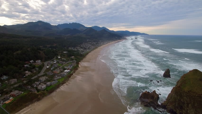 Aerial Panning Shot Of Haystack Rock In Sea By Residential Coastal City Under Cloudy Sky - Cannon Beach, Oregon Royalty-Free Stock Footage #3427443297
