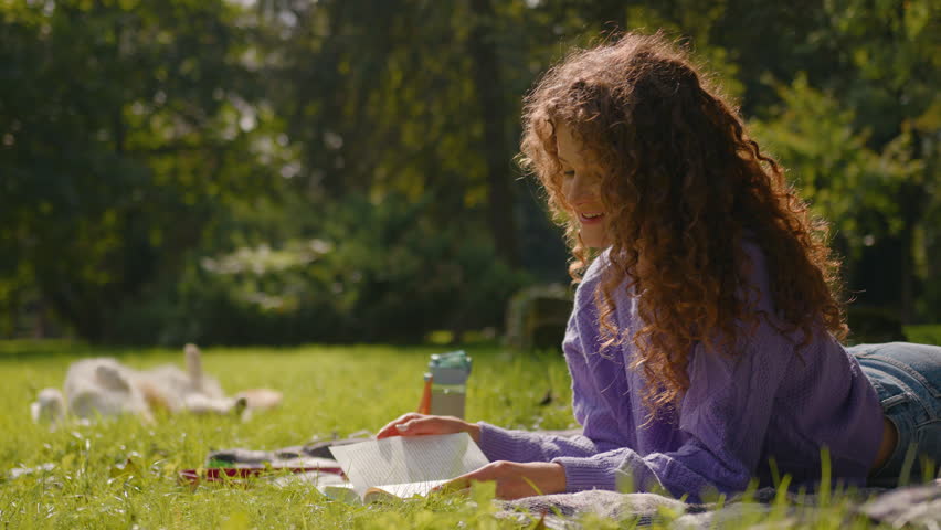 Caucasian happy smiling young joyful woman female student relax read book while little funny dog corgi puppy roll on grass background meadow park nature girl reading literature outdoors summer weekend Royalty-Free Stock Footage #3427444087