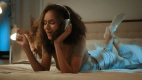 Relaxed happy African American ethnic girl singing song rest on cozy bed in wireless earphones young woman gen z teenager relax evening home listen music with headphones mobile phone holiday enjoying - Powered by Shutterstock - Get 15% off with code: PIKWIZARD15
