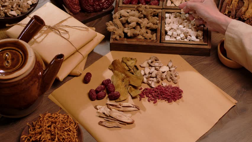 Close-up of a physician selecting each type of dry medicinal herb to put into a medicine package, next to a medicinal kettle on a wooden table. Traditional Chinese medicine.