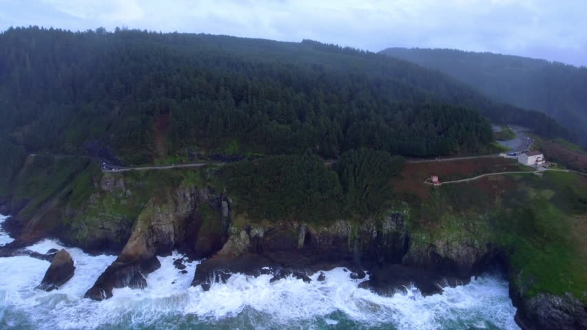 Aerial Panning Shot Of Trees On Hiking Trail Under Clouds, Drone Flying Over Wavy Ocean - Shore Acres, Oregon
