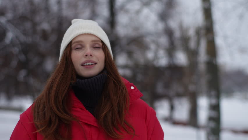 Cheerful relaxed young woman breathing deeply fresh air at winter cold frosty day with eyes closed, meditating, doing breath exercise. Happy lady with frosty breathing enjoying cold weather outdoors