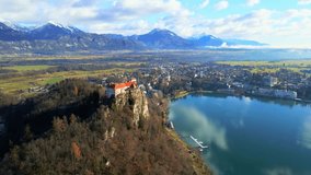 Stunning 4K aerial drone video captures Lake Bled, Slovenia, at sunrise. Shot in late autumn with snow-capped Julian Alps as a backdrop. Iconic Castle Bled standning on a cliff overviewing the lake.