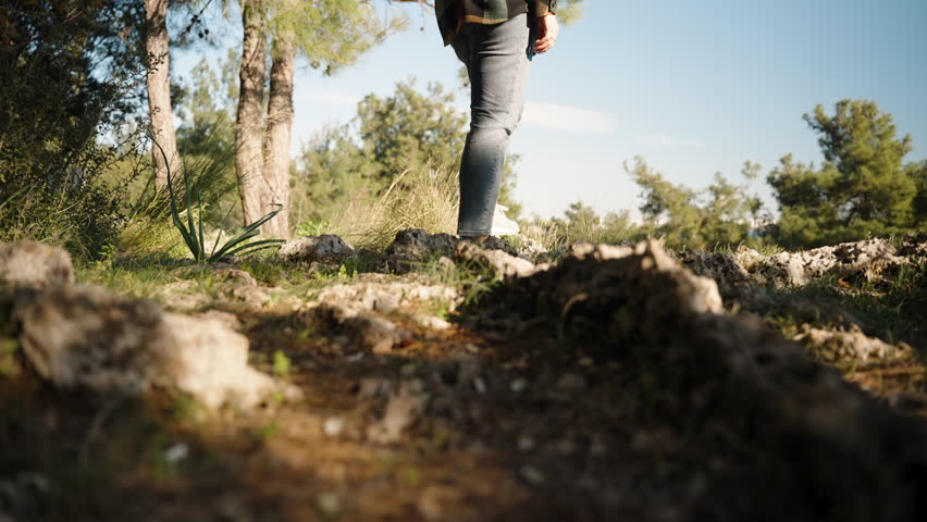 A young woman with a backpack in the forest, enjoying the view from a high cliff with the sea and pine trees in the background.