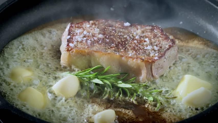Juicy piece of steak fried in butter on a pan with rosemary and garlic.Hot bubbling butter in a pan. 4k Slow motion video, 100fps.