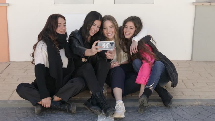 happy female friends sitting together taking photos with a smartphone