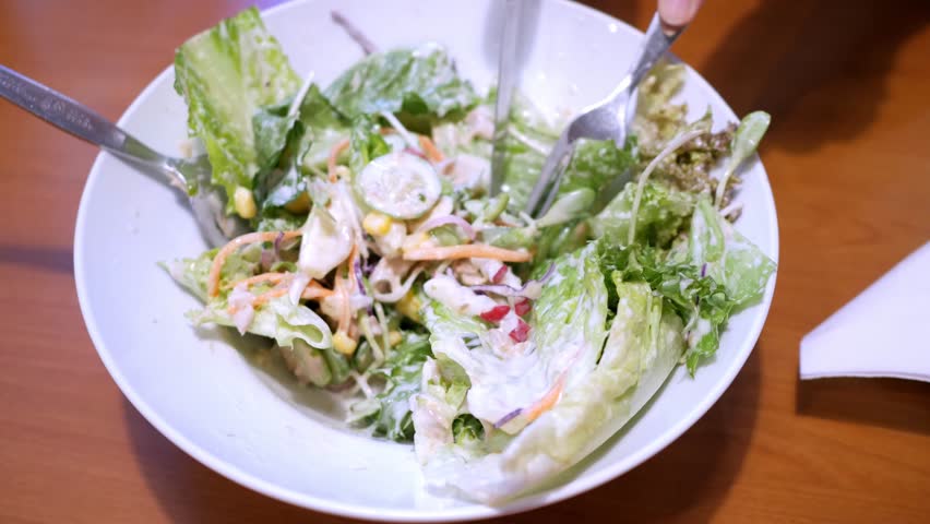 Cutting some salad greens into smaller bite-size cuts using a knife and a fork, in a restaurant in Bangkok, Thailand.