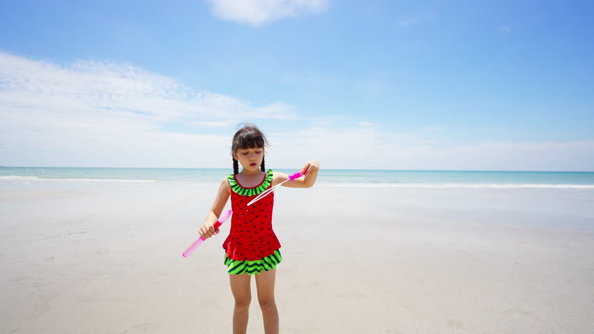 Happy Children travel playing at the sea on summer beach holiday vacation. Little cute Asian child girl kid in swimwear enjoy and fun outdoor lifestyle playing bubble wand at tropical island beach.