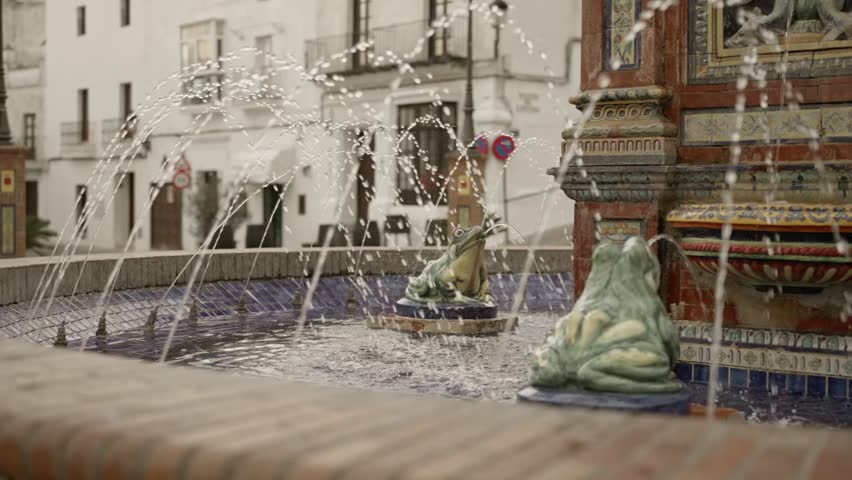 Scenic view of traditional fountain with frog statues spewing water up, residential buildings in background.