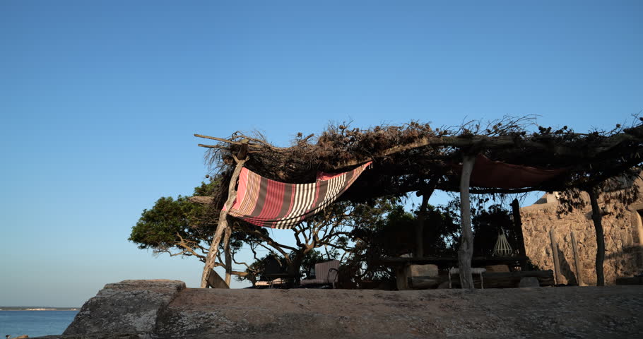 A hammock hangs from a tree, positioned close to a building, creating a cozy and relaxing outdoor resting spot.