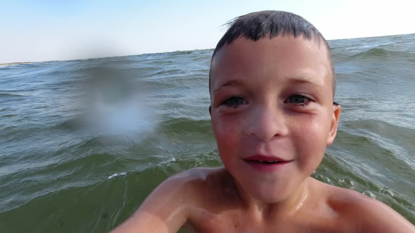 A boy dives into sea water while looking at the camera.