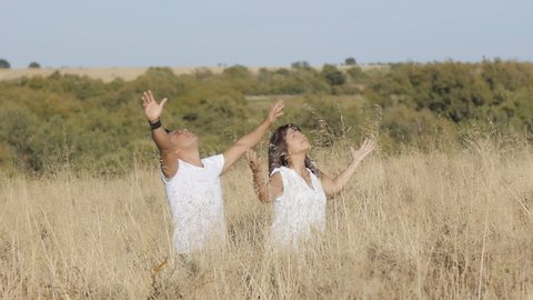 Praying concept.. A man and a woman in white clothes stand in grass stretching their arms up.