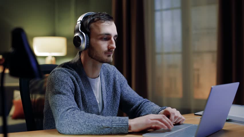 Attractive male freelancer listening to favorite songs on modern laptop with headphones. Positive man enjoying music while sitting at home, indoors, with closed eyes. Technologies and leisure time. Royalty-Free Stock Footage #3427845785