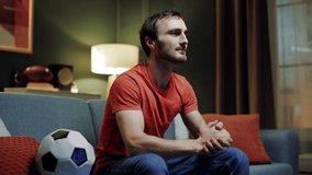 Handsome bearded man sitting alone in living room, football fan loving soccer cheering on football team on couch. Sports enthusiast unwinding in evening while watching sports station on television.