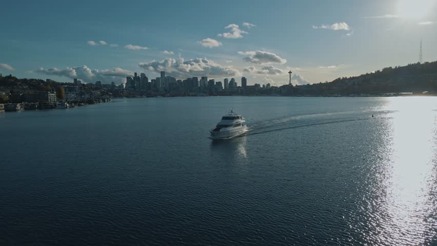 Yacht cruises slowly across waters of Lake Union with Seattle skyline behind on sunny day