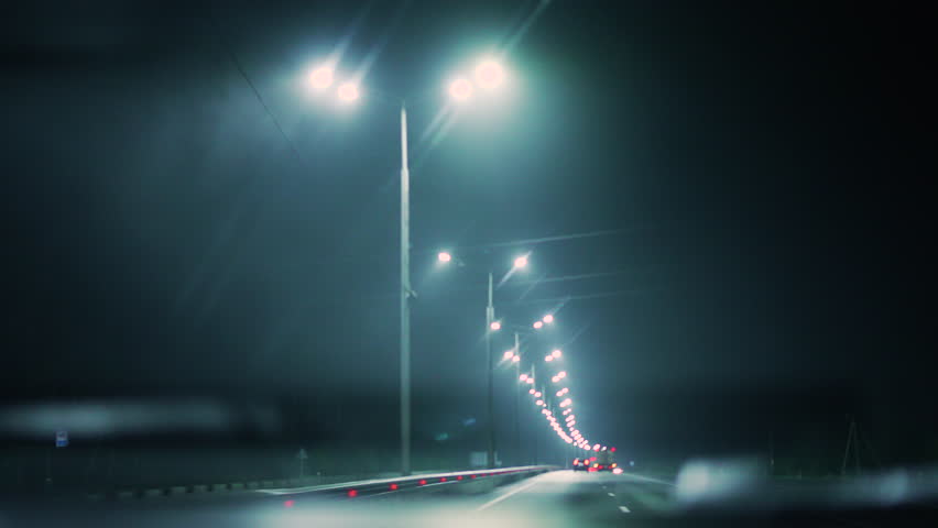 Driving a car at night in the fog along a highway illuminated by lanterns. Desolate night road brightly lit by a sequence of street lamps, with space traffic