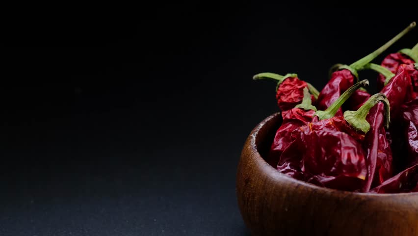 
Dried chili peppers in a wooden plate on a black background.Spices.