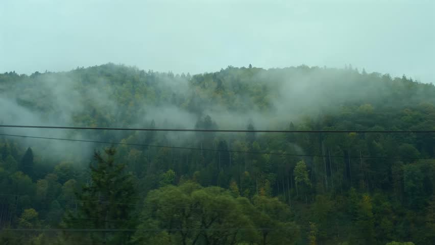 Mountains view outside train window. Passenger train compartment passing by railway bridge and electric wires, Mountain peaks in the morning fog. Traveling by train, nature of Ukraine