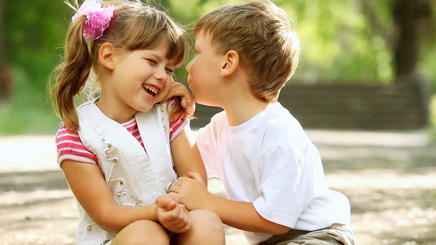Two children telling secrets and laughing in park, outdoors. dolly shot.