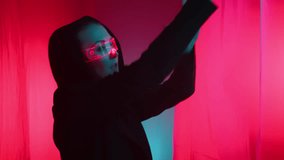 Amidst a crimson art space with fluttering curtains, a girl with red-lit tech glasses moves gracefully, her form a silhouette against the monochrome red background. High quality 4k footage