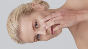 Studio portrait of young, beautiful and natural blond woman applying skin care cream. Vertical video. the concept of face lifting, cosmetics and make-up.