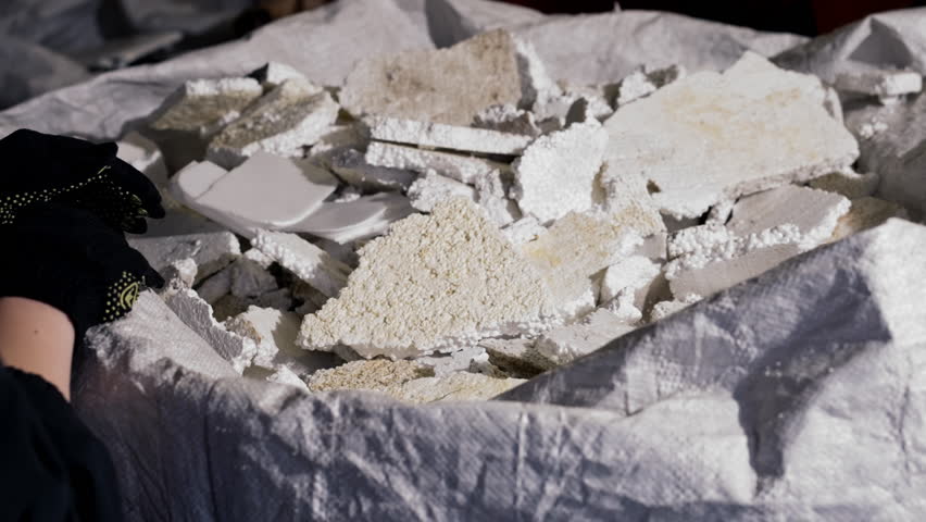 Close-up of a lot of styrofoam lying in a big bag at a waste recycling plant or sorting station a gloved hand takes it care for environment