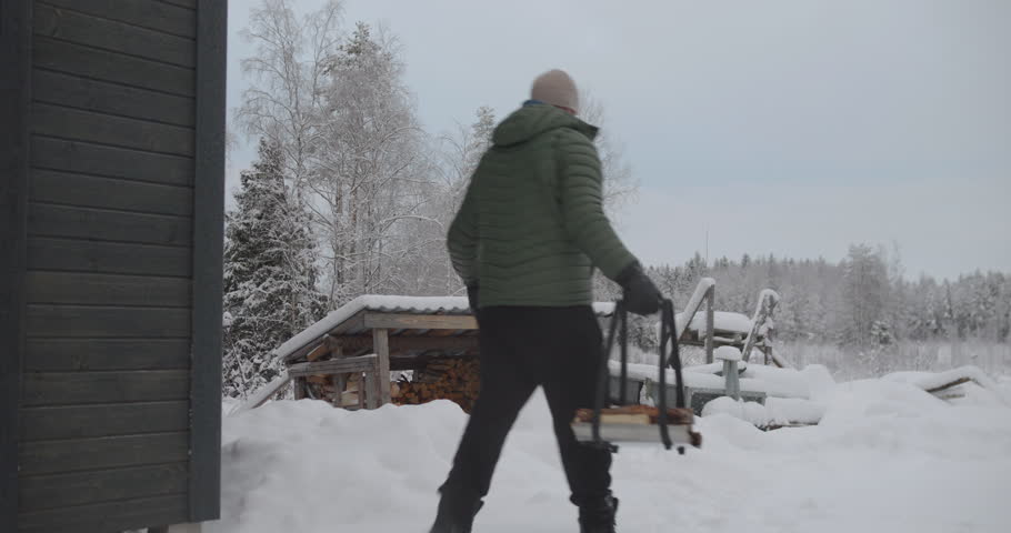 Man fetches wood in front of his house. Static view. Daylight