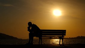 Silhouette of a pensive man at sunset. A man sits alone on a bench by the sea against the backdrop of a summer sunset. - Powered by Shutterstock - Get 15% off with code: PIKWIZARD15