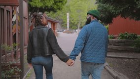 Back view of a diverse African American couple holding hands and walking down a peaceful street, with rustic cabins and lush greenery around. Slow Motion, Camera 4K RAW.  - Powered by Shutterstock - Get 15% off with code: PIKWIZARD15