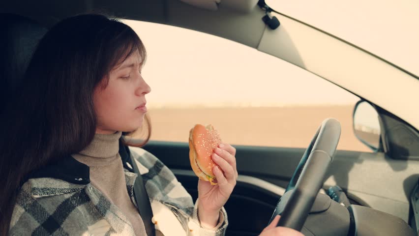 Woman driver travels, having snack Fast food on road in car, Young hungry woman eats roll with meatball while sitting in car. Girl passenger eats burger in car. Delicious food bun with cutlet. Tourist Royalty-Free Stock Footage #3428242691