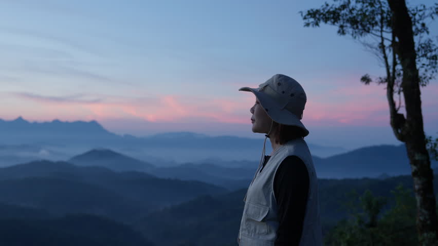 Asian happy tourist admire the mountainside scenery with hat and casual clothes and she smiles with her arms outstretched, enjoying nature. summer vacation trip on annual holiday, sun rises in morning Royalty-Free Stock Footage #3428260081
