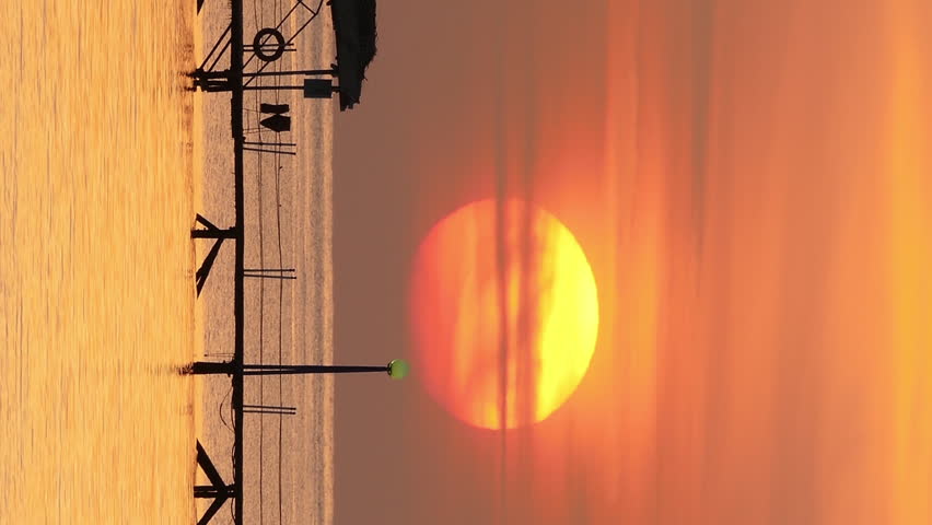 Beautiful sunrise over pier in sea - filmed at telephoto lens. Vertical video