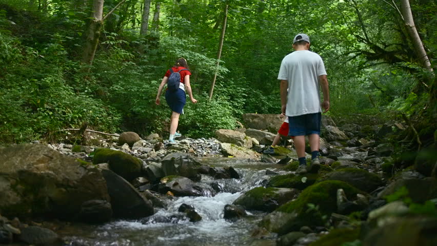 Family of mother and two boys jumping rocks across creek. Creative. Young travelers hiking together in North Carolina woods.