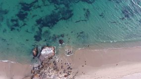 Tropical beach video loop showing seamless never ending footage with aerial bird eye view of green foaming ocean waves crushing against big rocks and a sandy beach with a seldom bird flying across