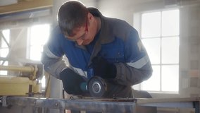 Slow motion video. Overall plan. Working man in overalls works with angle grinder in workshop. Mechanic removes old paint from metal surface. Cinematic light.