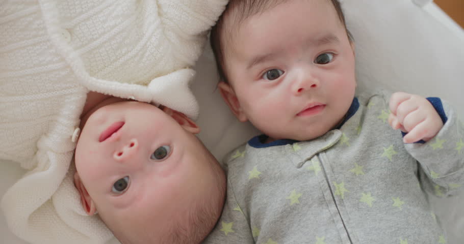 Cute little newborn twins boy and girl lie in bed smiling happily. Two caucasian babies brother and sister lying together in the bedroom at home. Happy family childhood positive kid bedtime lifestyle.