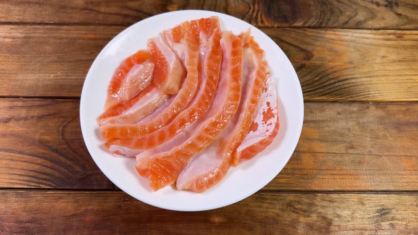 Salted salmon bellies strips without skin on the white dish on a rustic table, top view while rotation
