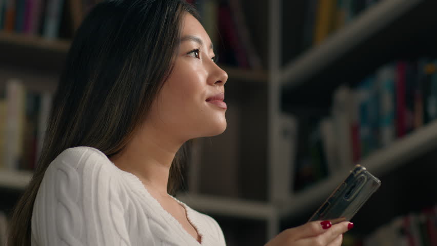 Asian woman female ethnic girl student searching book in university library on bookshelf using phone task list checking lesson schedule use mobile application on smartphone modern technology education Royalty-Free Stock Footage #3428619441
