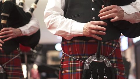 A man in a Scottish kilt is playing on a bagpipe. Concert. Bagpipes. A man in checkered clothes. Musician at the concert.