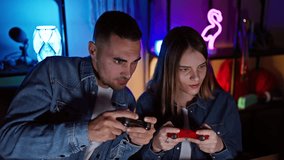 A man and woman intensely play video games together in a neon-lit home gaming room at night.