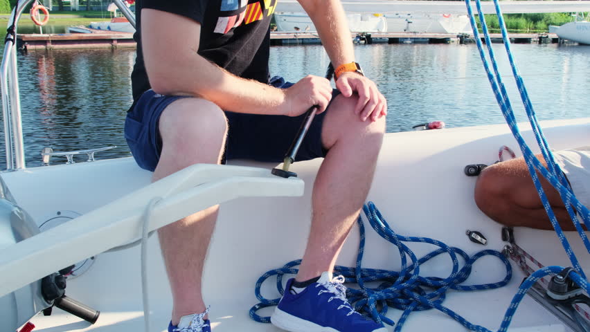Experienced skipper controls sailboat course using tiller. Yachtsmen enjoy manual steering control technique in calm water