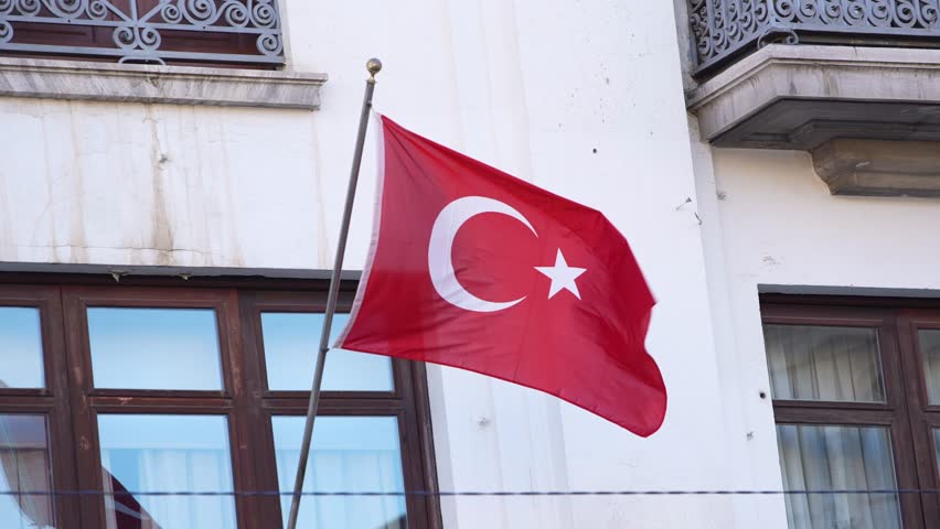 Slowmotion of a Turkish flag waving in the wind at traditional house with windows. Turkey banner blowing, soft and smooth silk. Cloth fabric texture ensign background. National day country concept