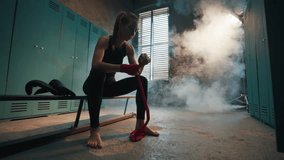 Young woman fighter boxer wraps hands wrists with boxing bandage in locker room. Focused girl kickboxer prepares for battle fight sits on bench. Professional sport, competition, preparation battle. - Powered by Shutterstock - Get 15% off with code: PIKWIZARD15