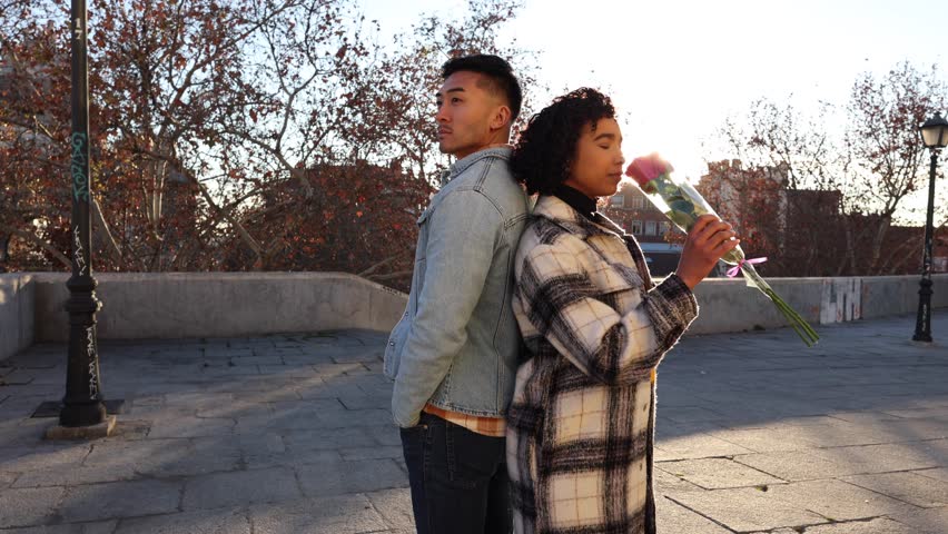 American shot of multiracial couple leaning back to back while the woman is smelling a bouquet of roses and the man is leaning on her with his eyes closed - Valentine