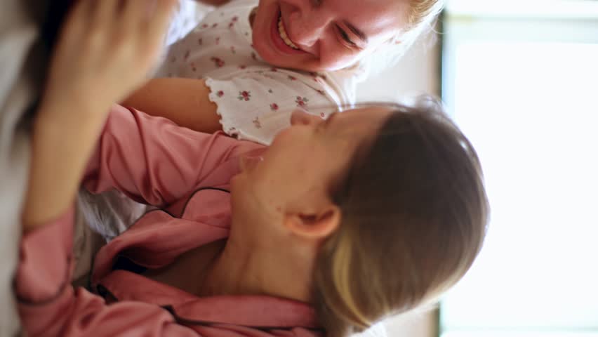 two sisters girlfriends blondes in pajamas lie in bed laughing and filling in writing a diary. sisterhood vertical video