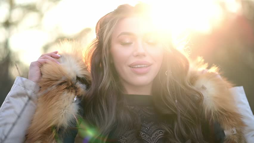 portrait of a sexy girl in a hood made of natural fur. Young woman in the rays of sunset in winter
