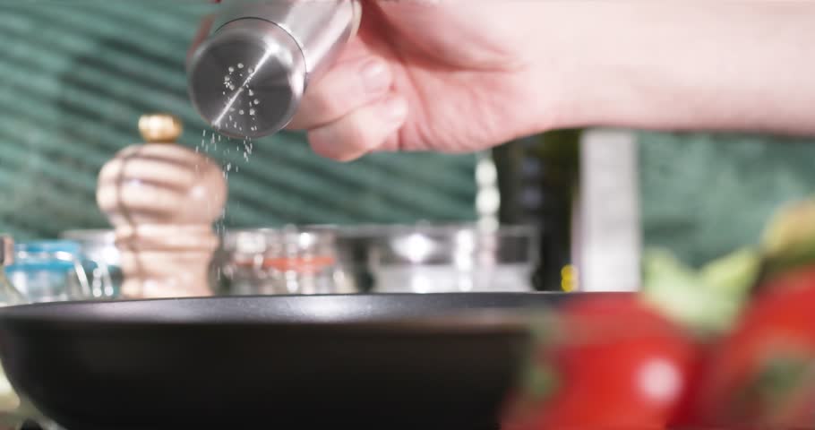 Sprinkling salt into the frying pan on a nearly cooked dish. Royalty-Free Stock Footage #3428947533